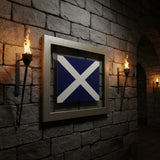 Framed flag with a blue background and white cross on a wooden wall.