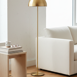 Gold floor lamp next to a white sofa and wooden side table with books and glasses.